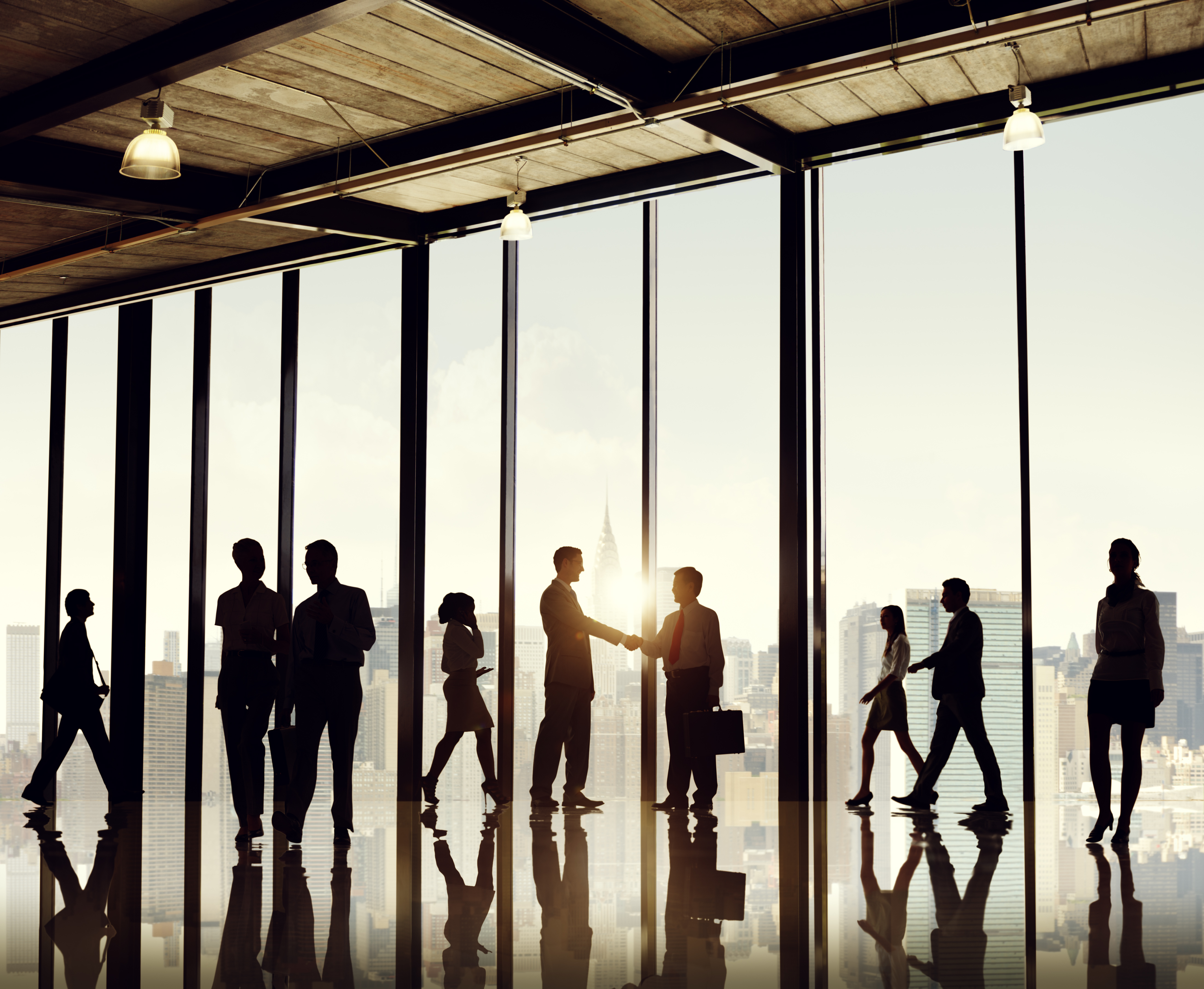 Silhouettes of business people walking, talking, and shaking hands with glass windows and a view of a cityscape in the background.