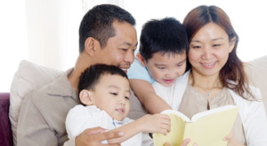 Asian-American family reading book on a couch.